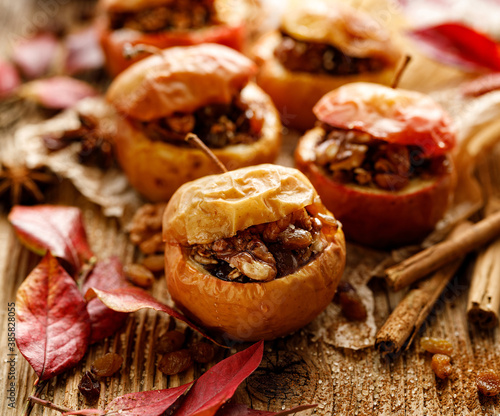 Baked apples stuffed with nuts, raisins and honey, seasoned with cinnamon on a wooden table, close up view. Delicious autumn dessert