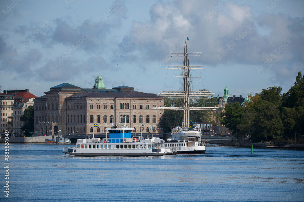 Commuter boats a new and a old version of Djurgårdsfärja and hostel full rigged ship af Chapman in the harbor of Stockholm at the island Skeppsholmen a sunny summer day in Stockholm