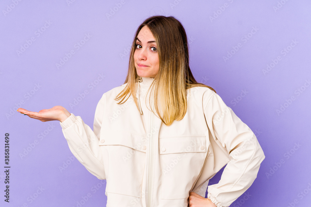 Young caucasian woman isolated on purple background doubting and shrugging shoulders in questioning gesture. Young caucasian woman isolated on purple background doubting and shrugging shoulders in questioning gesture.