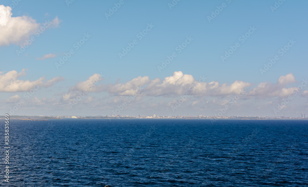 Fototapeta premium White cumulus clouds in sky over blue water of Gulf of Finland landscape, with vague silhouette of Finland in the horizon. Big cloud above sea.