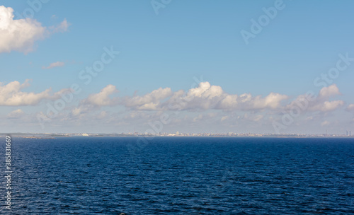 White cumulus clouds in sky over blue water of Gulf of Finland landscape, with vague silhouette of Finland in the horizon. Big cloud above sea.