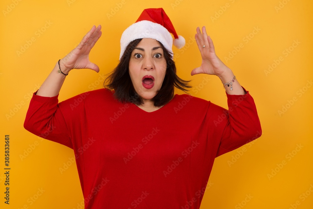 Portrait of beautiful brunette female standing against yellow background, looks with excitement at camera, keeps hands raised over head, notices something unexpected. Portrait of beautiful brunette female standing against yellow background, looks with excitement at camera, keeps hands raised over head, notices something unexpected.