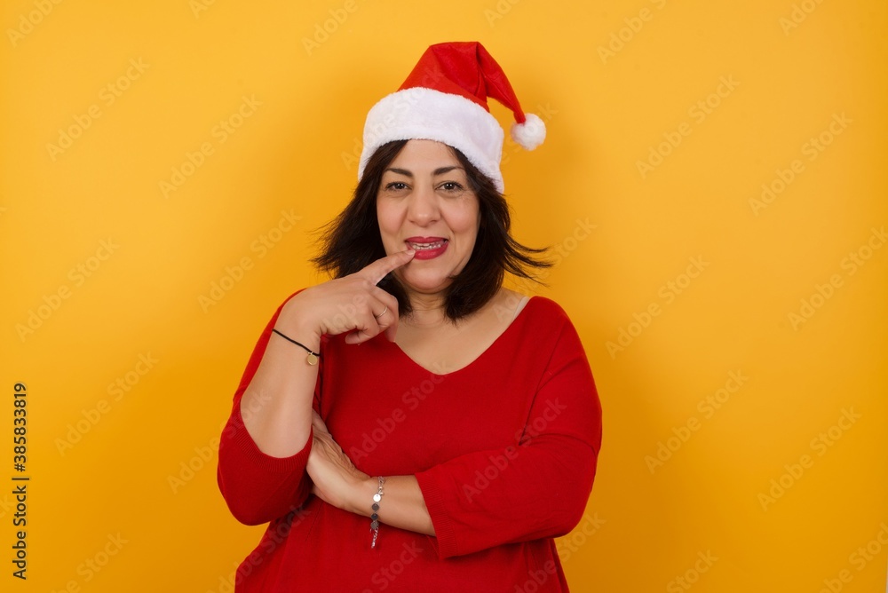 Dreamy female with thoughtful expression, looks to the camera, keeps hand near face, bitting a finger thinks about something pleasant, poses against gray wall. Dreamy female with thoughtful expression, looks to the camera, keeps hand near face, bitting a finger thinks about something pleasant, poses against gray wall.