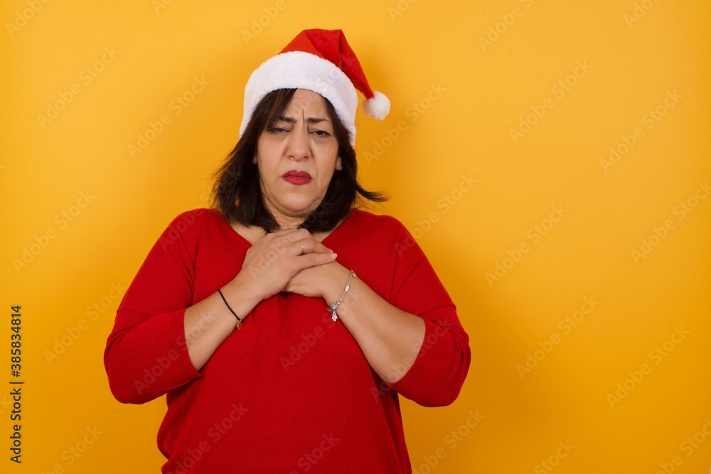 Sad pretty middle aged woman wearing Santa hat feeling upset while spending time at home alone staring at camera with unhappy or regretful look standing outdoors. Sad pretty middle aged woman wearing Santa hat feeling upset while spending time at home alone staring at camera with unhappy or regretful look standing outdoors.