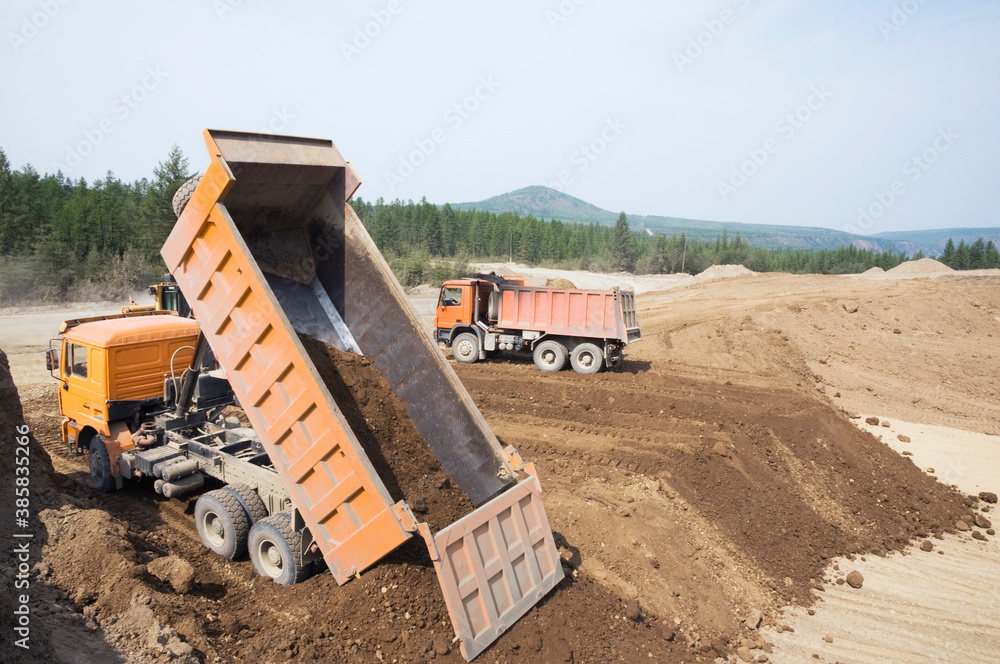 A dump truck unloads clay on a sunny summer day.