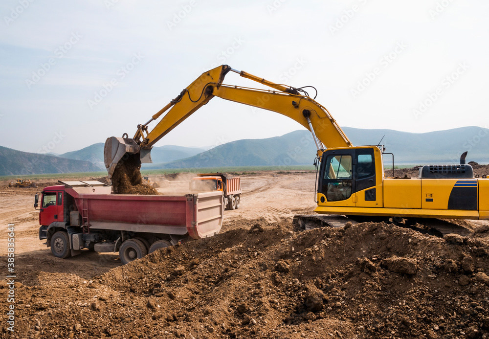 Excavator loads clay into the body of a dump truck on a sunny summer day Excavator loads clay into the body of a dump truck on a sunny summer day