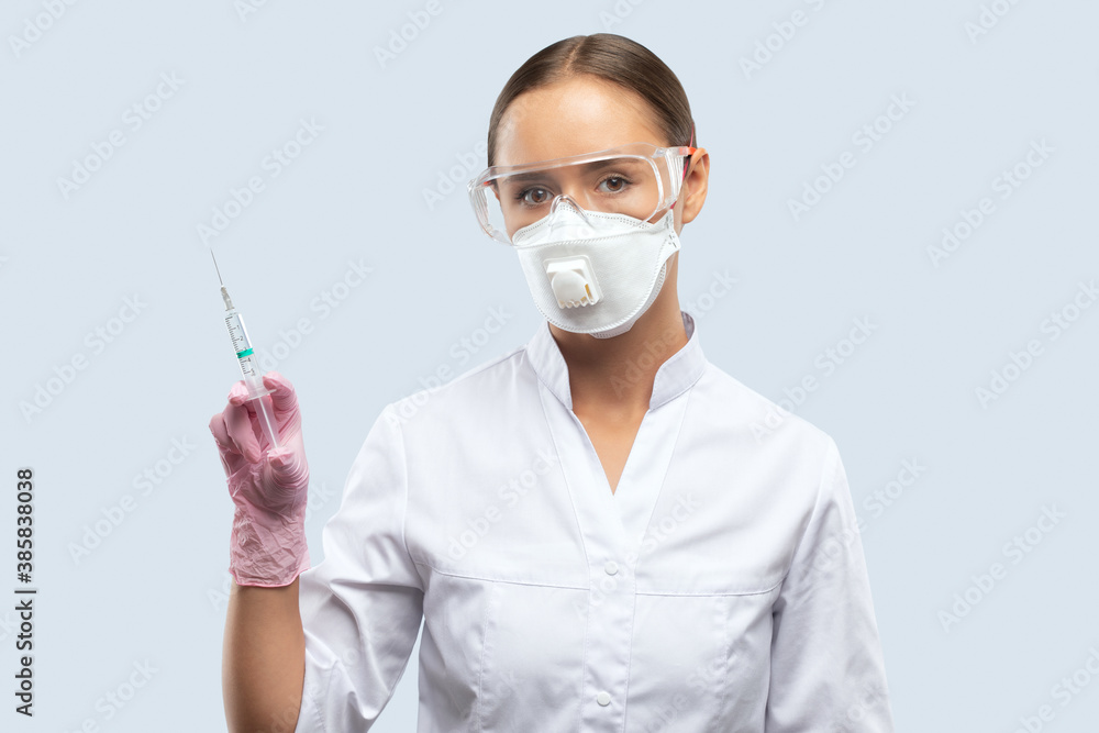 A doctor in a white coat, a face mask and goggles, rubber gloves holds a syringe with a vaccine in her hand. Medical concept, Covid-19. A doctor in a white coat, a face mask and goggles, rubber gloves holds a syringe with a vaccine in her hand. Medical concept, Covid-19.