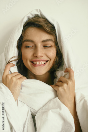 Portrait of young beautiful girl with blanket on white background. At home. Comfort. Healthy lifestyle, clear skin. Curly hair. Emotions. About sleeping and awakening.