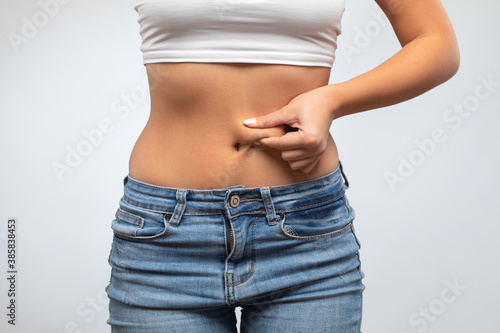 Girl pulls the skin on the abdomen, showing the body fat in the abdominal area and sides. Treatment and disposal of excess weight, the deposition of subcutaneous fat. © Dimid