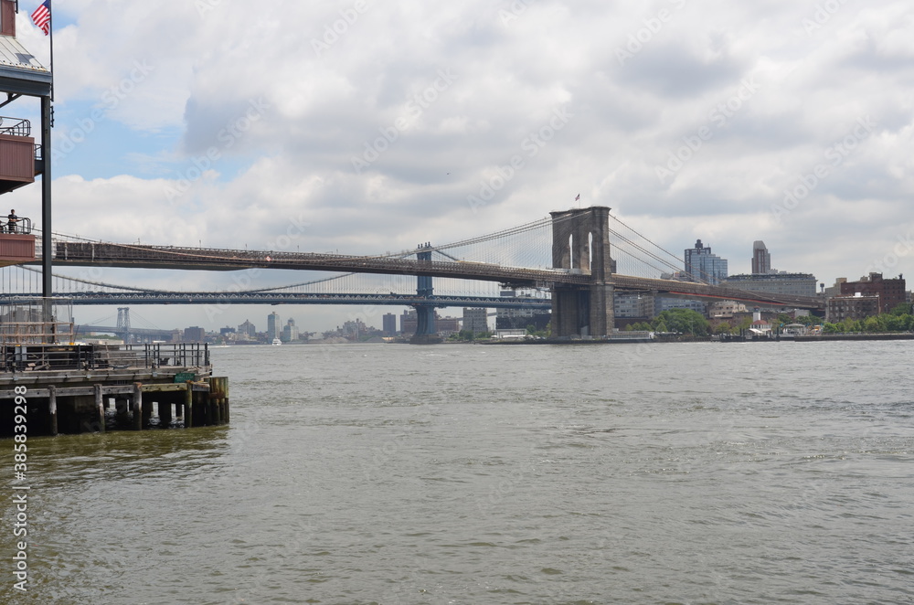 View of the Brooklyn Bridge over the Hudson River in New York with skyline in the background under cloudy skies