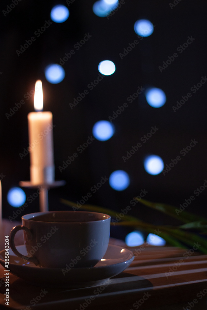 Fototapeta premium Tea cup on a dark table with candle and bokeh lights in a dark background