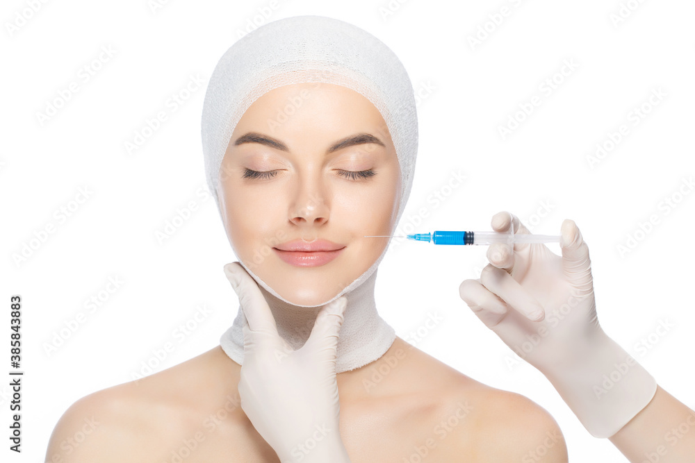 Young beautiful woman with head wrap, prepared for syringe injection into skin by beautician with closed eyes, isolated on white background. Young beautiful woman with head wrap, prepared for syringe injection into skin by beautician with closed eyes, isolated on white background.