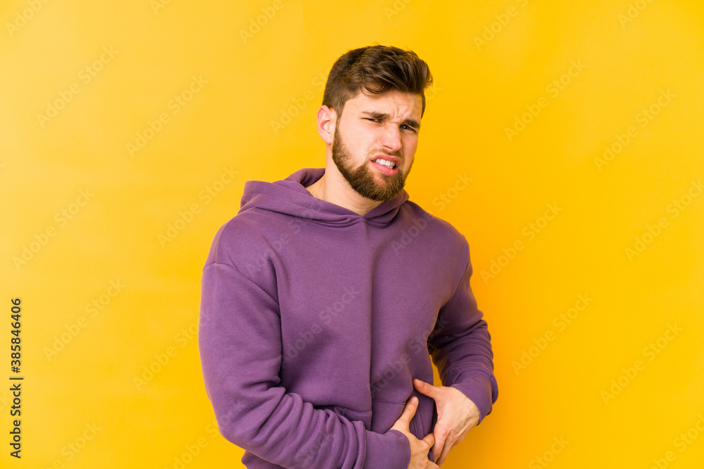 Young caucasian man isolated on yellow background having a liver pain, stomach ache. Young caucasian man isolated on yellow background having a liver pain, stomach ache.
