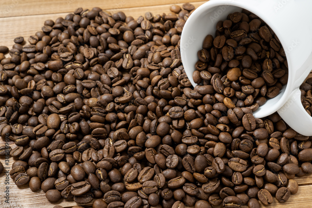 Fototapeta premium Coffee beans spilled from a cup on a wooden table.