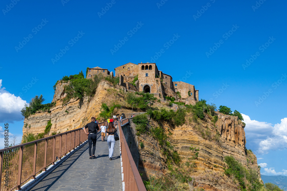 Civita di Bagnoregio. A young couple is crossing the bridge to reach the town set in the clouds, known as The Dying Town, on the top a plateau of volcanic tuff, Lazio Italy.