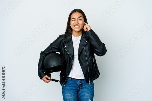 Young asian woman holding a motorbike helmet over isolated background covering ears with hands.