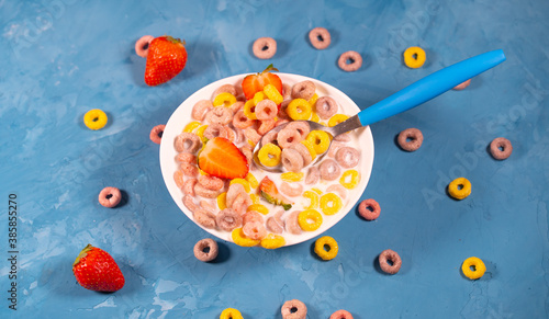 Healthy breakfast with cereal and berries. From above of bowl with delicious healthy breakfast made with colorful cereal rings and fresh strawberry with milk served on blue table