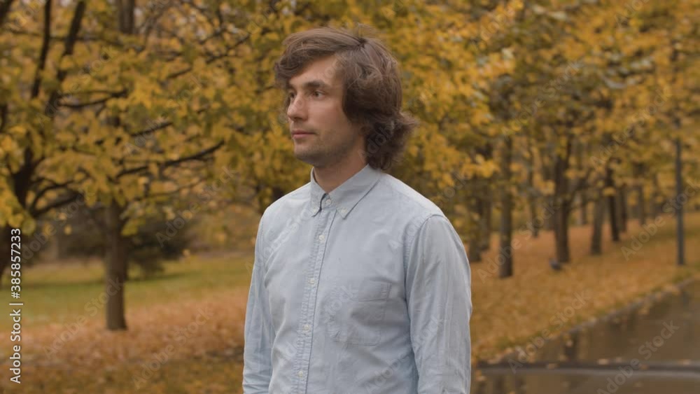 Portrait of young handsome man standing in the autumn park under the rain. Yellow leaves on the trees. Autumn day in the city, steadicam shot Portrait of young handsome man standing in the autumn park under the rain. Yellow leaves on the trees. Autumn day in the city, steadicam shot