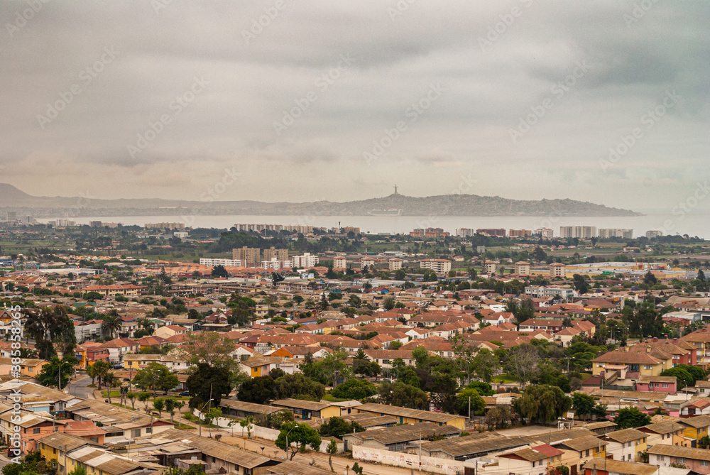 La Serena, Chile - December 7, 2008: Bird eyes view over part of downtown with bay of Coquimbo and mountains on horizon under brown cloudscape. Millennium cross in distance. House roofs and green foli