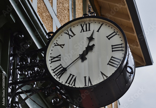 Macro View of Round Black Outdoor Clock with Roman Numerals Mounted on Building Under Roof