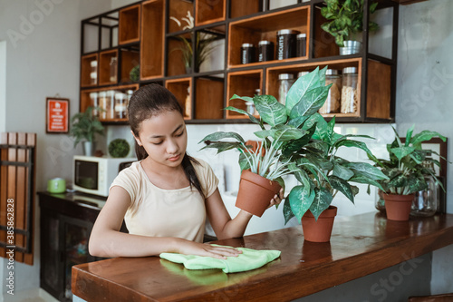 a beautiful young girl cleaning the kitchen with a cloth and holding a pot at home photo