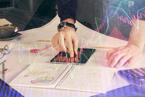 Double exposure of man's hands holding and using a digital device and forex graph drawing. Financial market concept.