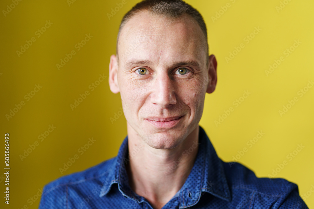 Obraz premium Front view close up portrait of male adult caucasian man with short blonde hair and green eyes in front of yellow background looking to the camera smiling with copy space