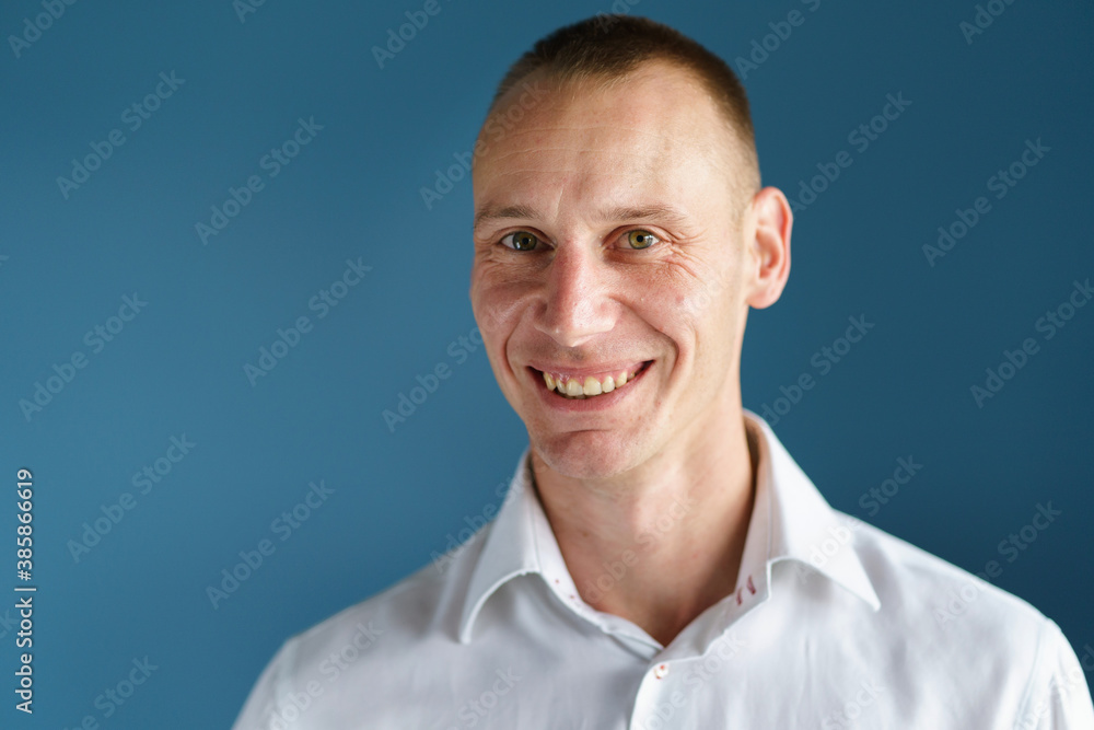 Front view close up portrait of male adult caucasian man with short blonde hair and green eyes in front of blue background looking to the camera smiling with copy space Front view close up portrait of male adult caucasian man with short blonde hair and green eyes in front of blue background looking to the camera smiling with copy space