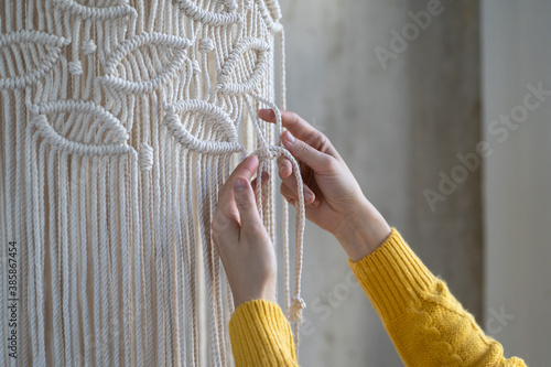 Close up of freelancer woman working on half-finished macrame piece, weaves lamp shade for chandelier. Women hobby. photo