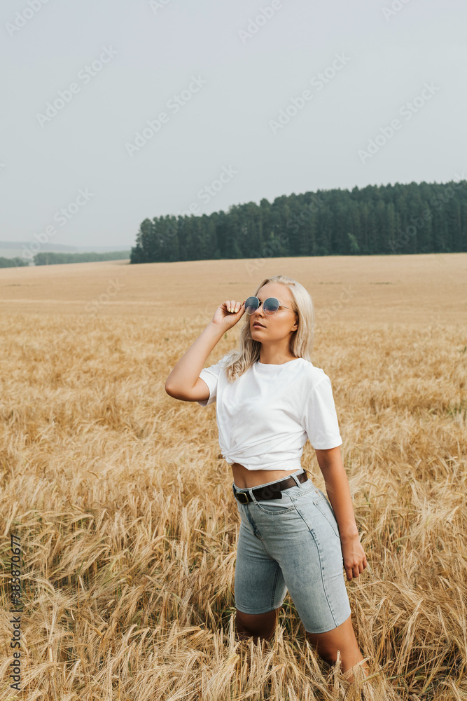 Woman in a white T-shirt and shorts in the field. blonde woman in sunglasses. A beautiful fit tanned girl. Sexy slim model outdoors. . High quality photo Woman in a white T-shirt and shorts in the field. blonde woman in sunglasses. A beautiful fit tanned girl. Sexy slim model outdoors. . High quality photo