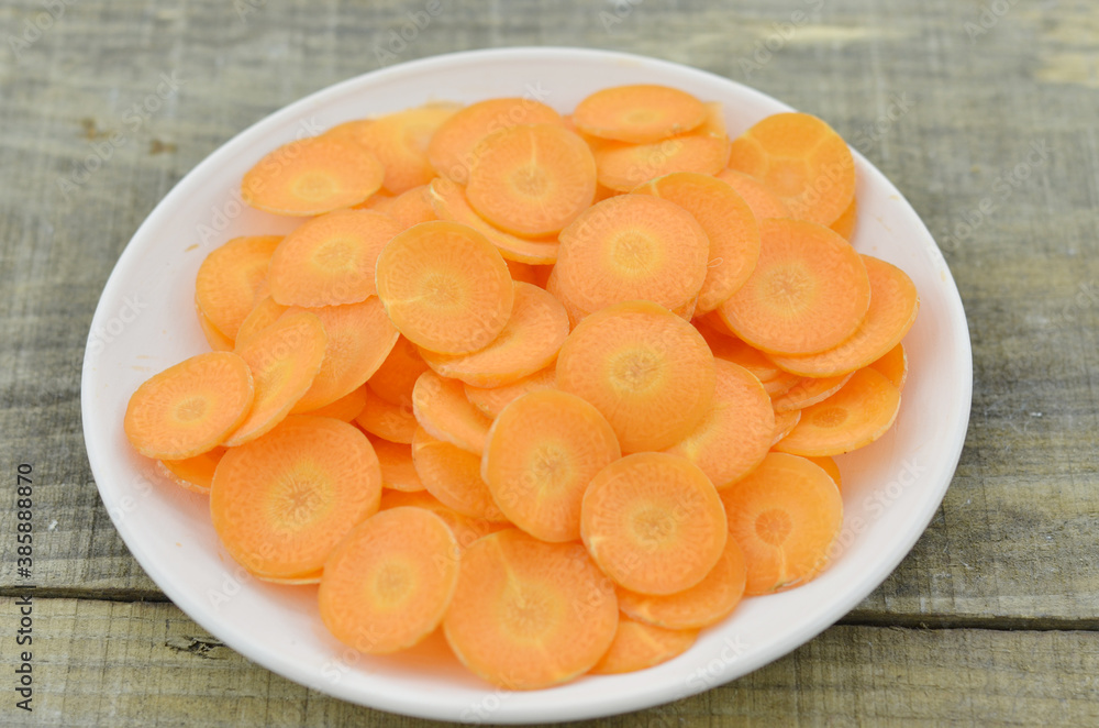White plate with fresh thin slices carrots on wooden table, closeup White plate with fresh thin slices carrots on wooden table, closeup