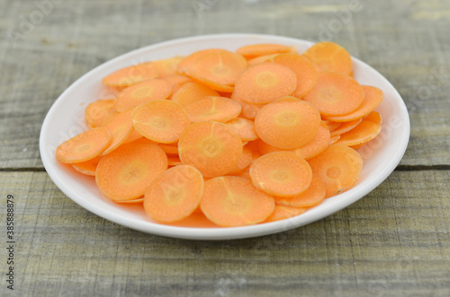 White plate with fresh thin slices carrots on wooden background, closeup
