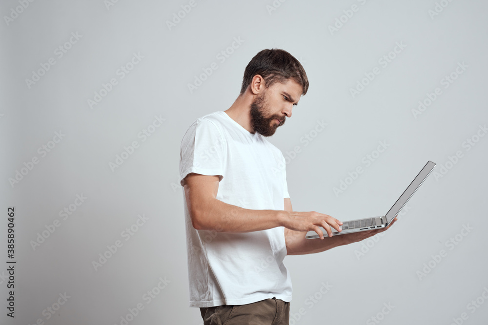 A man with a laptop in his hands on a light background in a white t-shirt emotions light background new technologies A man with a laptop in his hands on a light background in a white t-shirt emotions light background new technologies