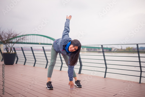 Young woman stretching before run. Cloudy day near river.