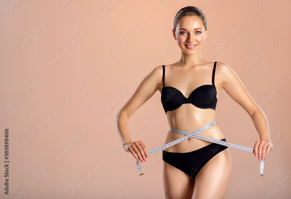 Fototapeta premium Young smiling woman with tape and a beautiful, healthy body. Sexy woman measuring her perfect body.