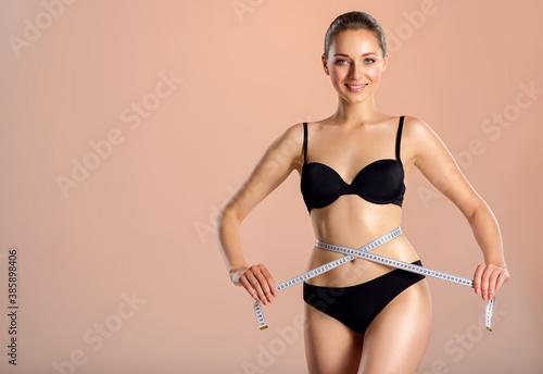 Young smiling woman with tape and a beautiful, healthy body. Sexy woman measuring her perfect body.