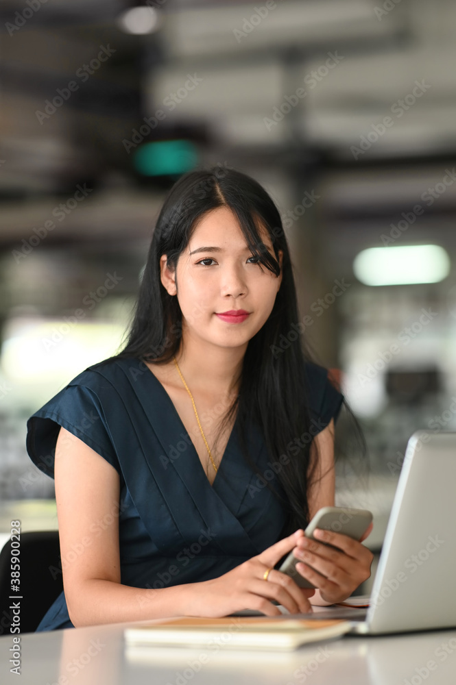 Portrait of female fleelance using smart phone and laptop on her work space.