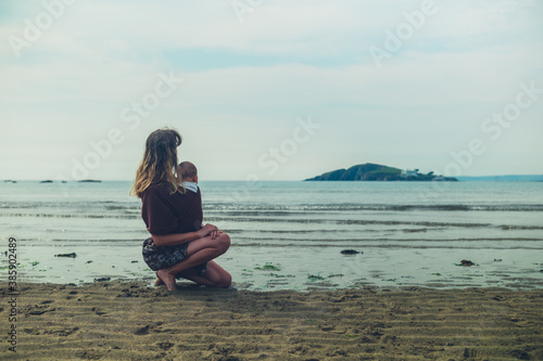 Young mother resting on the beach with her baby in slling © LoloStock