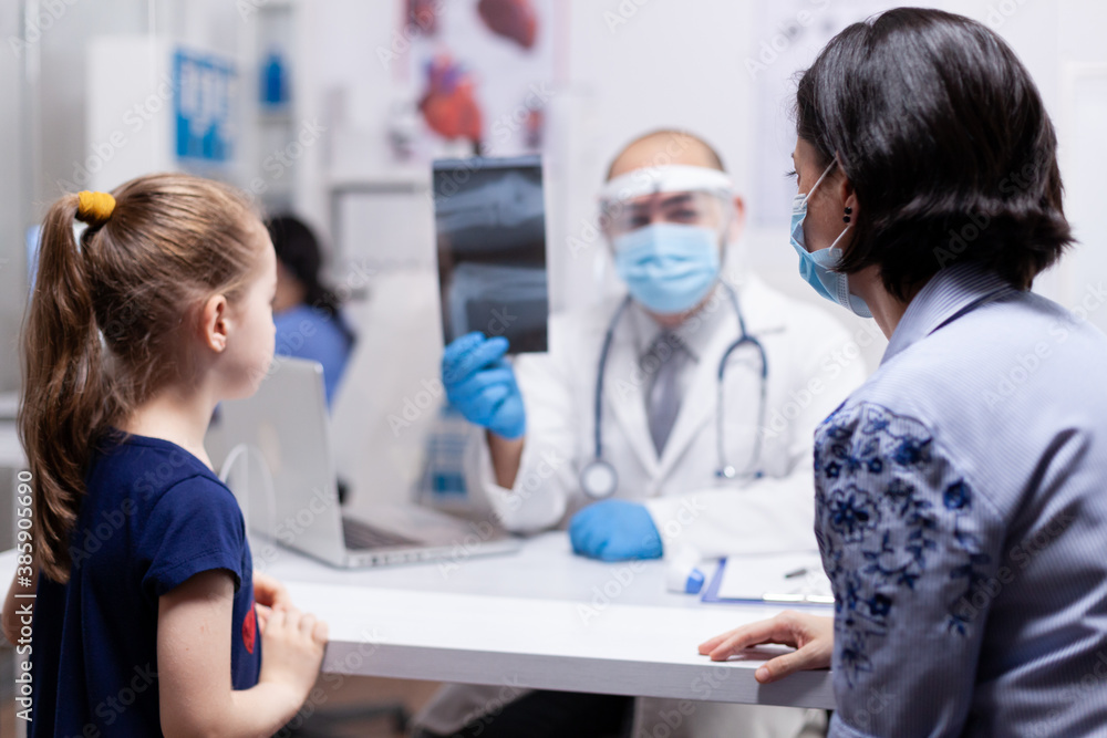 Mother with child at doctor consultation during coronavirus global pandemic. Pediatrician specialist with protection mask providing health care service radiographic treatment examination