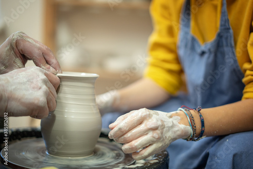 Woman learning to make ceramic utensils in a workshop at lesson with a teacher on a potter s wheel  hands in clay close-up