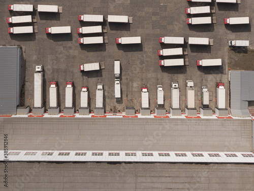 Aerial Top View of White Semi Truck with Cargo Trailer Parking with Other Trucks on Special Parking Lot.