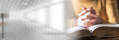 Woman praying with her hands over the bible, hard light; panoramic banner