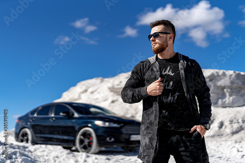 Wallpaper Mural Stylish bearded young man on front view. Fashion clothes and trandy sunglasses. Luxury black car on background. White high rocks landscape. Torontodigital.ca