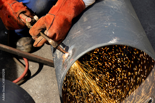 Photos Welder worker welding a wide metal pipe tube with a oxy-fuel cutting torch, with