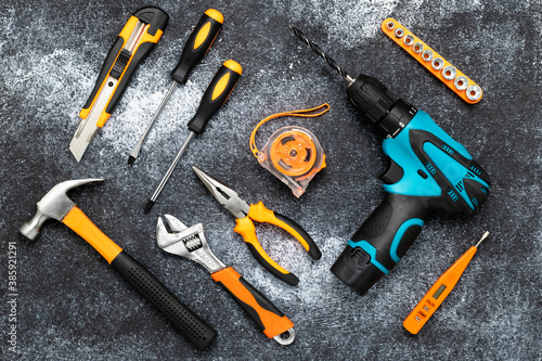 A set of tools for home renovation, a collection of instruments on a black board background. Flat lay. DIY concept. Electric drill, pliers, screwdriver, tape measure, wrench, knife and сlaw hammer.