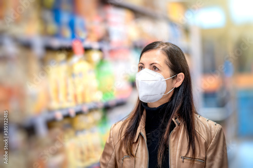 Woman in a protective mask with a cart during a coronavirus pandemic stands choosing food in the grocery store