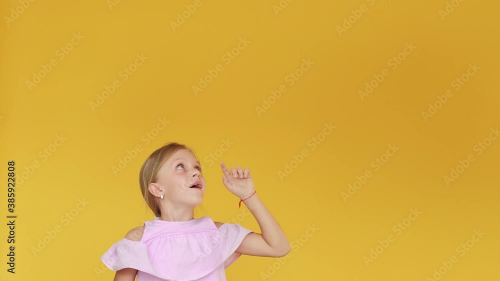 Special offer. Inspired child. Choice decision. Virtual game. Amused little girl in pink summer dress pointing up at invisible options isolated on orange empty space background. Special offer. Inspired child. Choice decision. Virtual game. Amused little girl in pink summer dress pointing up at invisible options isolated on orange empty space background.