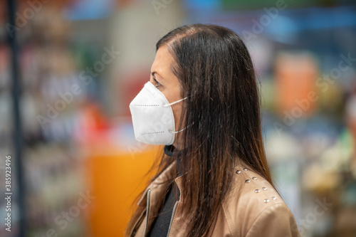 Woman in a protective mask with a cart during a coronavirus pandemic stands choosing food in the grocery store