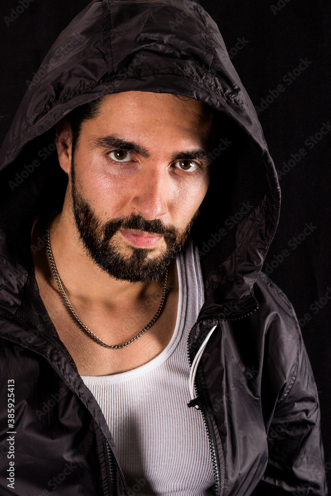 Dramatic portrait of handsome bearded man wearing dark hood looking at camera on a black background Dramatic portrait of handsome bearded man wearing dark hood looking at camera on a black background
