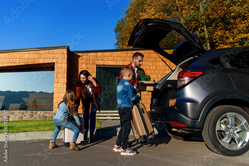 Obraz na plátně Joyful family helping each other to unload auto's trunk from carton boxes and su